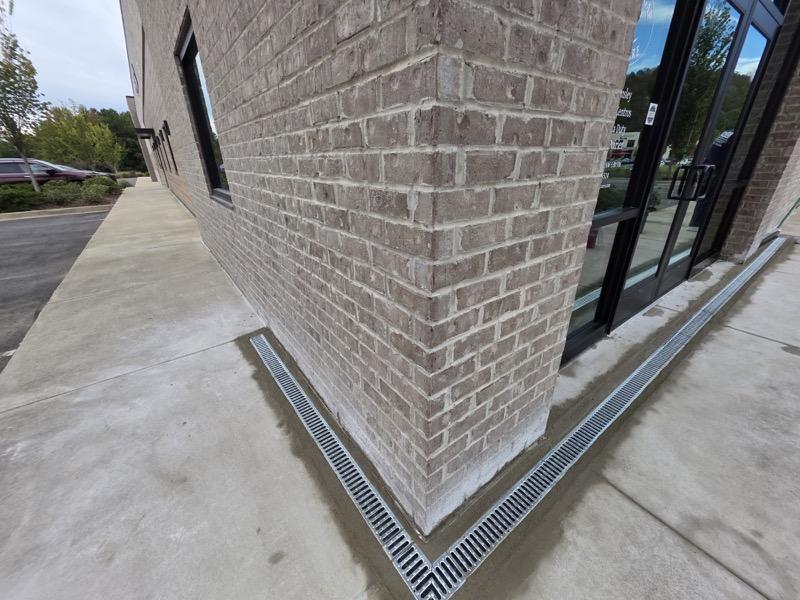 Brick commercial building corner with trench drains and glass storefront entrance on concrete sidewalk